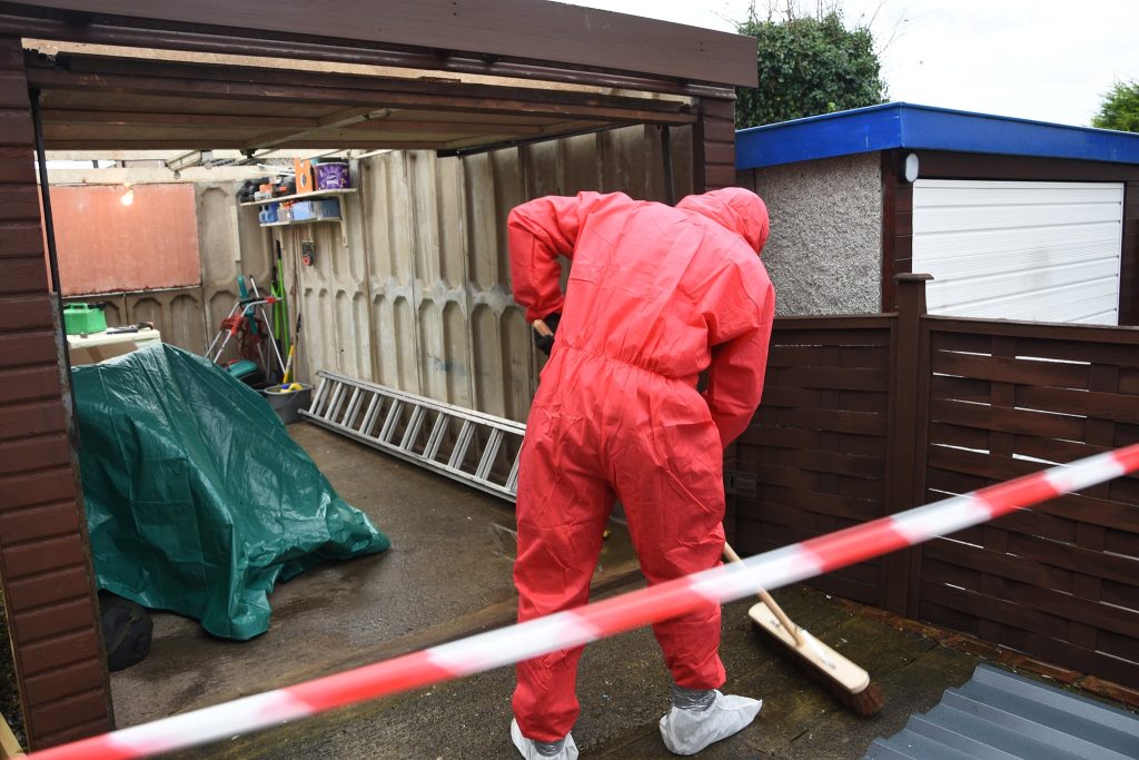 A man in a red suit sweeping a cluttered garage floor in Yorkshire.